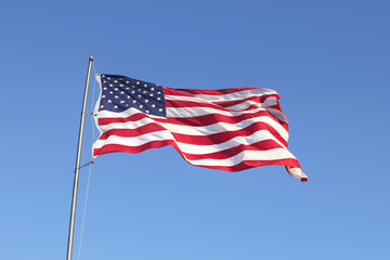 Fototapeta premium American Flag Fluttering: A vibrant image of the United States flag gracefully waving in the wind against a clear, azure sky, symbolizing freedom and national pride.