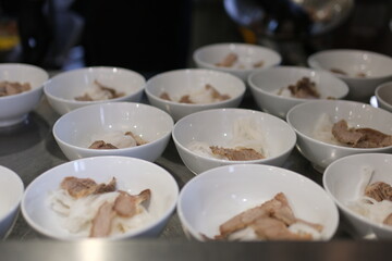 many white soup bowls in the buffet rice noodles and pieces of meat waiting to be poured with broth