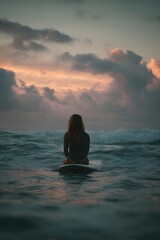 Fototapeta premium Surfer gazing at the sunset while sitting on a surfboard amidst gentle ocean waves and clouds