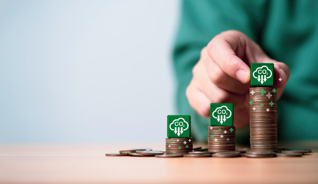 Businessman stacking CO2 reducing icon on increasing coins for decrease CO2 , carbon footprint and carbon credit to limit global warming from climate change and company profit concept.
