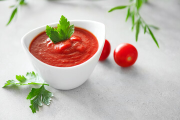 Tomato sauce, Homemade tomato paste in a white bowl and fresh ingredients on a grey table. Ketchup, Red sauce for pizza or pasta made from fresh bio tomatoes 