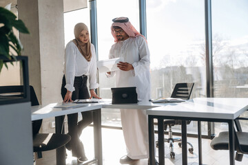 In traditional clothes. Muslim man and woman are indoors in modern building