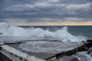 Stormy sea waves crashing against a rocky shore at sunset. Dark clouds fill the sky, creating a dramatic atmosphere. Copy space available for text.