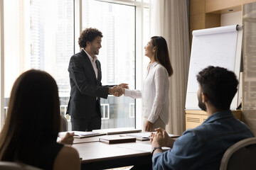 Best worker of the year. Proud smiling male corporate top manager ceo chief honoring smiling millennial Asian female clerk employee with handshaking on boardroom meeting with multiethnic staff group