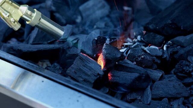 A person using a blowtorch to light charcoal in a grill