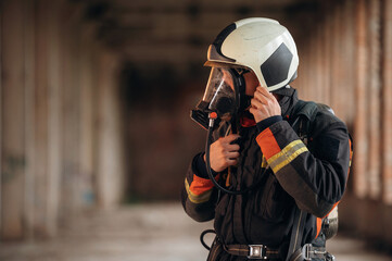 Standing in the abandoned building. Firefighter in professional equipment is indoors