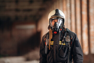 Protective air mask is on the face. Firefighter in professional equipment is indoors in abandoned...