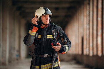 With walkie talkie radio. Firefighter in professional equipment is indoors in abandoned building