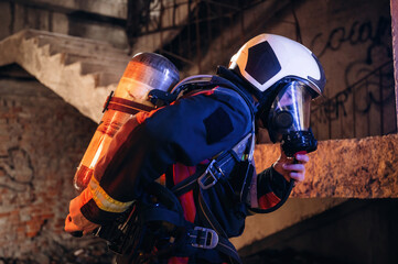 Obraz premium View from the side, with air balloons and mask. Firefighter in professional equipment is indoors in abandoned building