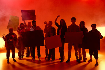 Protesters in red light wit fog hold posters and shout together. Some raise fists, others bang...