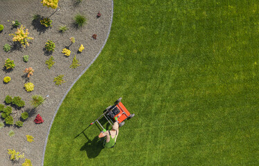 Man Mowing a Well-Maintained Lawn With a Gardening Tool in a Landscaped Yard During Sunny Daytime