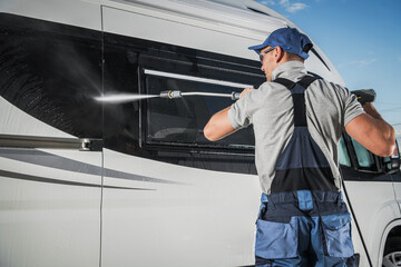 Man Washing a Camper Van With a Pressure Washer on a Sunny Day at an Outdoor Location