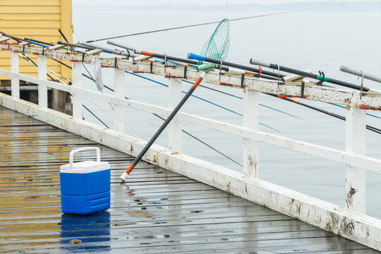 A small esky sitting on a jetty next to a row of fishing rods attached to the railing