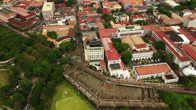Intramuros fortress wall borders red roofed historic buildings and tree lined streets in central Manila during an overcast daytime aerial view