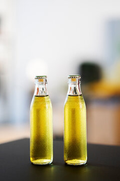 Two cold bottles of refreshing yellow beverage stand on a dark table. Condensation covers the glass, indicating they are chilled and ready to drink.