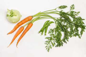 Carrots with long green tops. Pea pods and peeled peas. Kohlrabi cabbage on table.