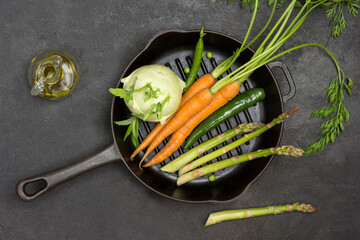 Fresh carrots with green tops, green pepper pod and asparagus in frying pan.