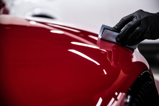 Detailer applying ceramic coating to a red car hood using an applicator pad.