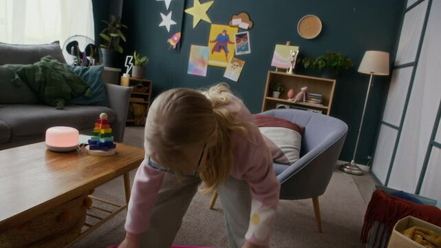Handheld shot of cute Caucasian girl doing hula hoop in cozy kids room with posters of superheroes in background