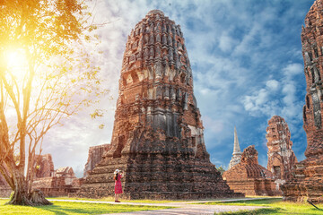 solo traveler concept. happy Asian woman tourist in red dress taking picture of old pagoda around history temple for cultural tourism at Ayutthaya World Heritage Site, Thailand