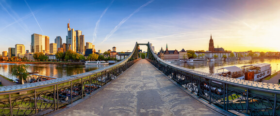 Panoramic view of the old iron bridge Eiserner Steg crossing the Main river in Frankfurt, Germany, with the skyline behind during summer sunrise