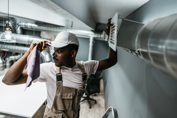 Maintenance worker performs air vent cleaning in modern office setting to ensure optimal air...