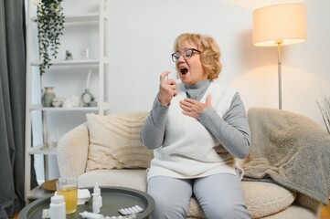 A woman is comfortably settled on her couch, using a soothing throat spray while surrounded by an...