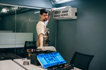 Technician installs air conditioning unit in modern office space during daylight hours