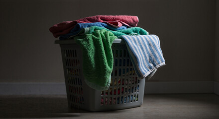 Laundry basket filled with colorful towels in dark room  