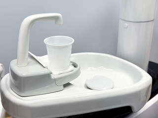 Modern dental equipment with cup on white sink against gray background