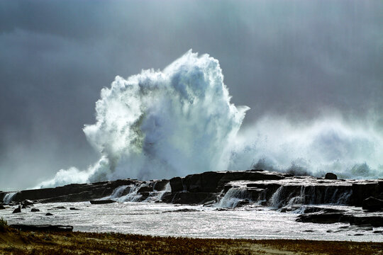A large swell smashes against a rocky headland under a stormy sky in Iluka, New South Wales