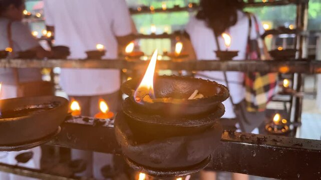 An oil lamp lit with a bright flame in a Buddhist temple, surrounded by other lamps in the background.
