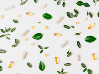 Various multivitamin capsules and green leaves scattered on a clean white background.
