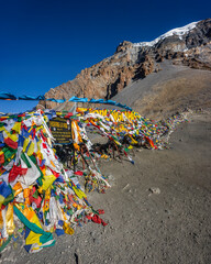 The waving prayer flags at the top of Thorung La Pass, the highest point of the Annapurna Circuit Trek in Himalaya mountains, Nepal, and Yakwakang peak on the horizon.