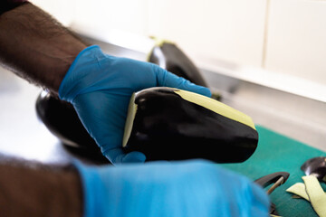 Close-up of hands in blue gloves peeling fresh eggplant on cutting board in small commercial kitchen