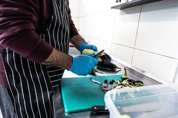 Chef in uniform peeling eggplant with peeler – small business kitchen and food prep concept