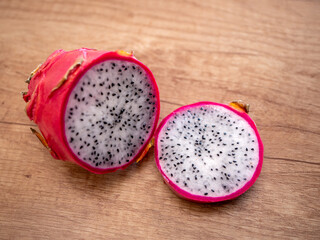 Sliced dragon fruit on wooden surface, showing white flesh with black seeds and pink skin. Exotic...