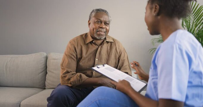 Nurse and Elderly Black Man Discuss His Healthcare Needs in His Living Room