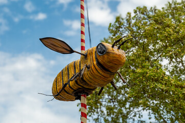 Giant handmade bee decoration brings joy to festival as colorful clouds drift above green trees