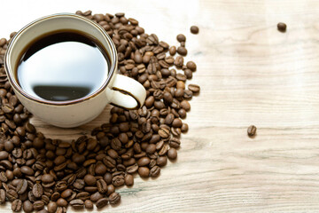 A cup of coffee stands in a pile of coffee beans on the left side of a wooden table. Perfect for coffee-themed design.