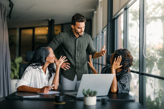 A manager frustrated addresses two employees during a work discussion in a modern office