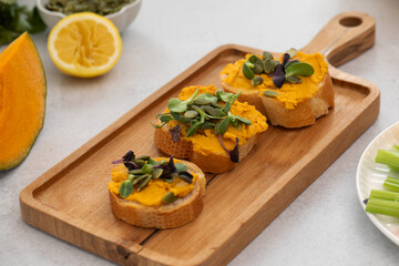 Delicious bruschetta with pumpkin hummus and microgreens on wooden board