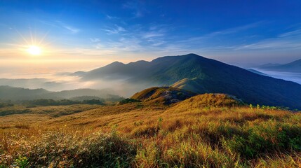 Sunlit distant mountains under green-blue sky with fog covering from base to peak. Panoramic wide-angle view in high-definition, natural lighting, warm tones, tranquil and magnificent scenery.