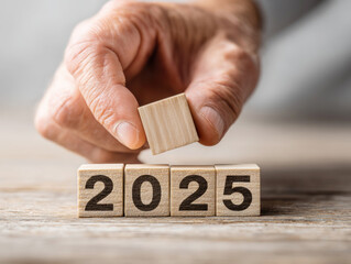 Hand placing wooden block with number 2025 on wooden table background