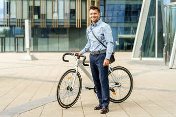 Businessman in a smart outfit rides his bicycle near a modern urban building during daytime