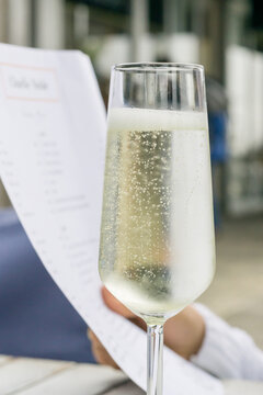 Close up of a glass of bubbly champagne with a menu being held behind