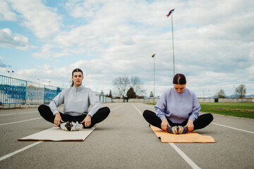 Two female friends stretching on stadium doing sport activities	
