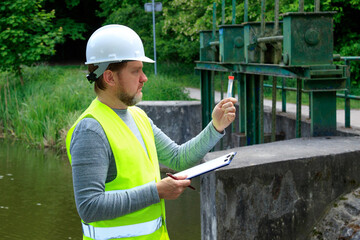 Ecologist man takes a sample of natural water near a hydro dam. Checking the quality of water....