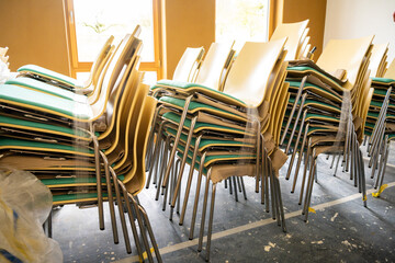 Stacks of stacking chairs with metal frames, beige backs, and green seats, wrapped in plastic for protection and storage.
