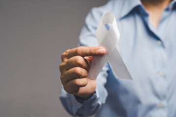Close-up hand with white ribbon in support of health awareness, prevention, and advocacy.